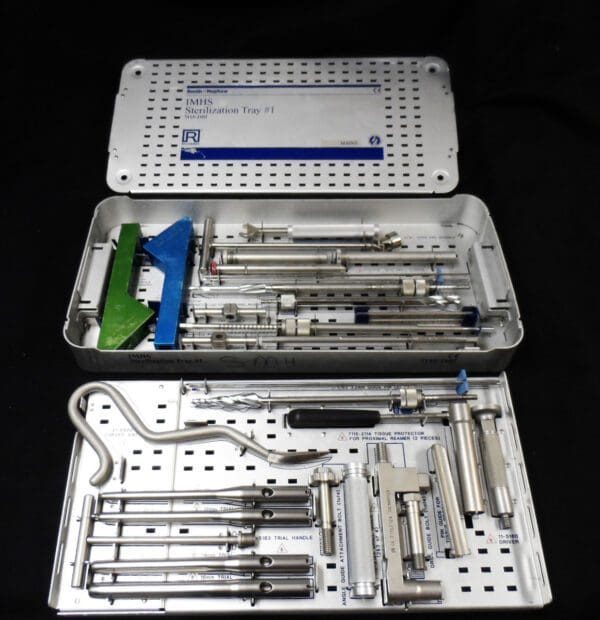 A set of surgical tools in a metal box on a black surface.